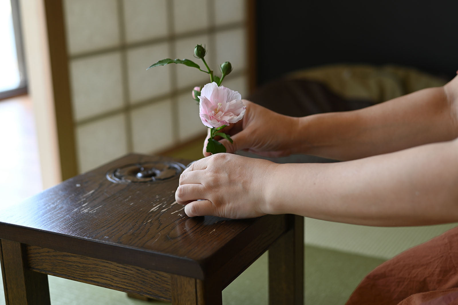 Room内の低い木のテーブルで、小さな花器に花を生ける手。