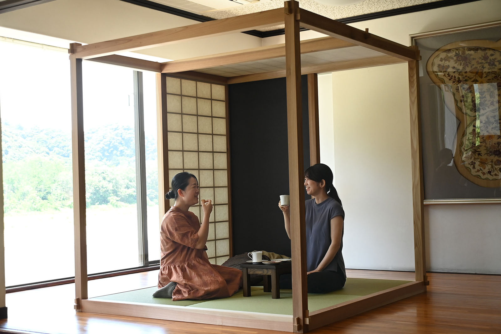 Room内の低いテーブルのそばに座り、カップを持つ二人の女性。
